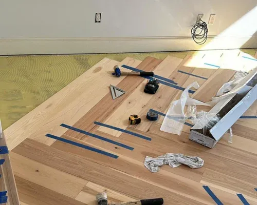 Layout tools and trim on a white oak floor mid-install